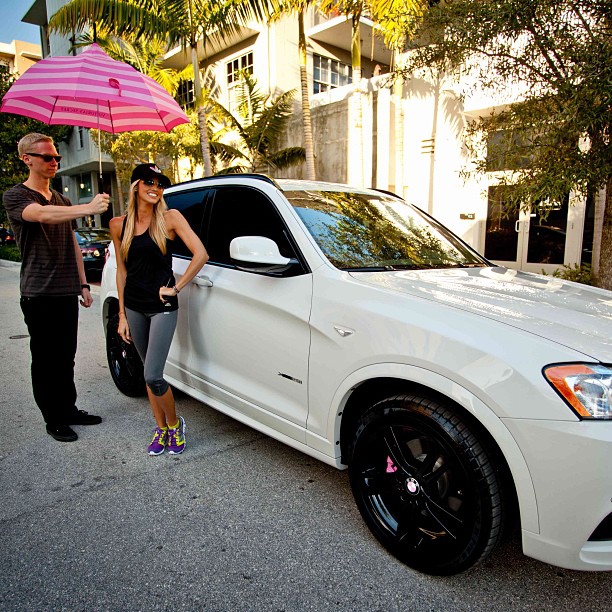 Lauren Tannehill and Ryan Tannehill under pink lined umbrella beside their car (BMW X4).